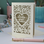 Personalised cut out wedding card with decorative patterns and names on a desk with stationery items.