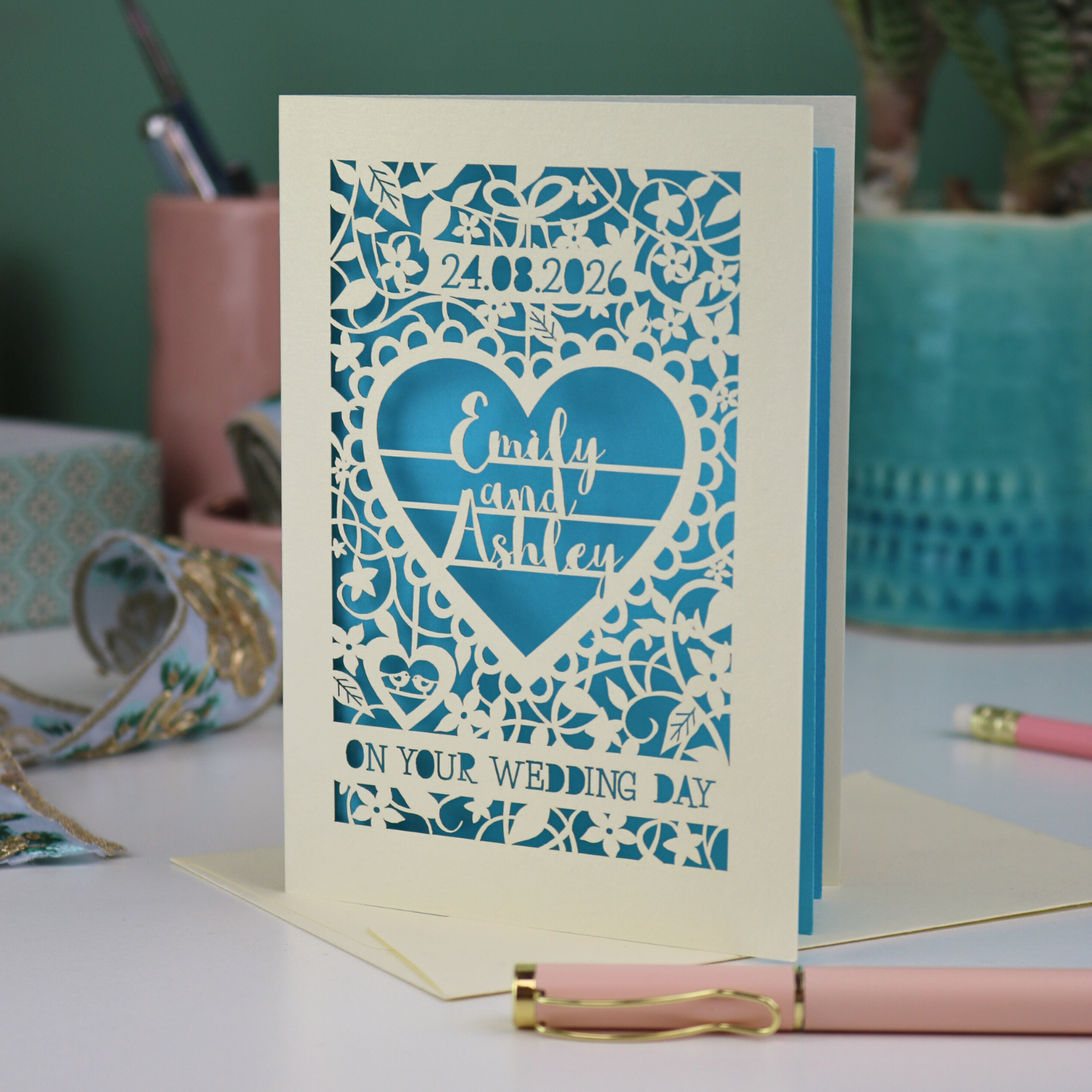 A laser cut on your wedding day card, personalised with a date and the names, standing on a white desk with stationery items