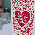 Laser-cut wedding invitation with a heart design and text on a blurred background