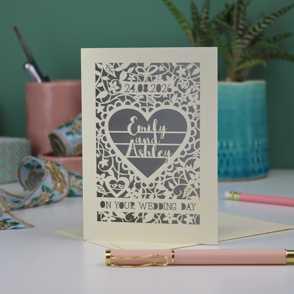 Laser-cut wedding card with personalized text on a table with stationery items.