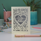 Laser-cut wedding card with personalized text on a table with stationery items.