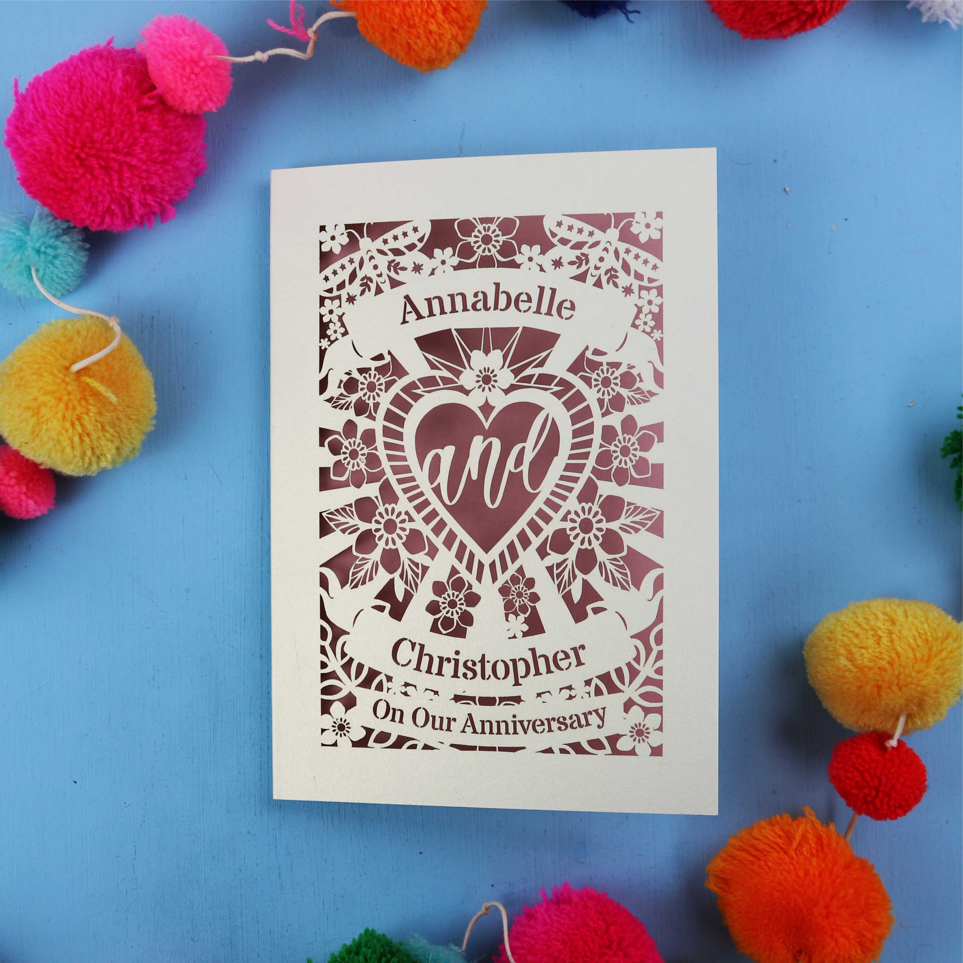 Personalised anniversary card with decorative heart design on a blue background with colourful pom-poms.