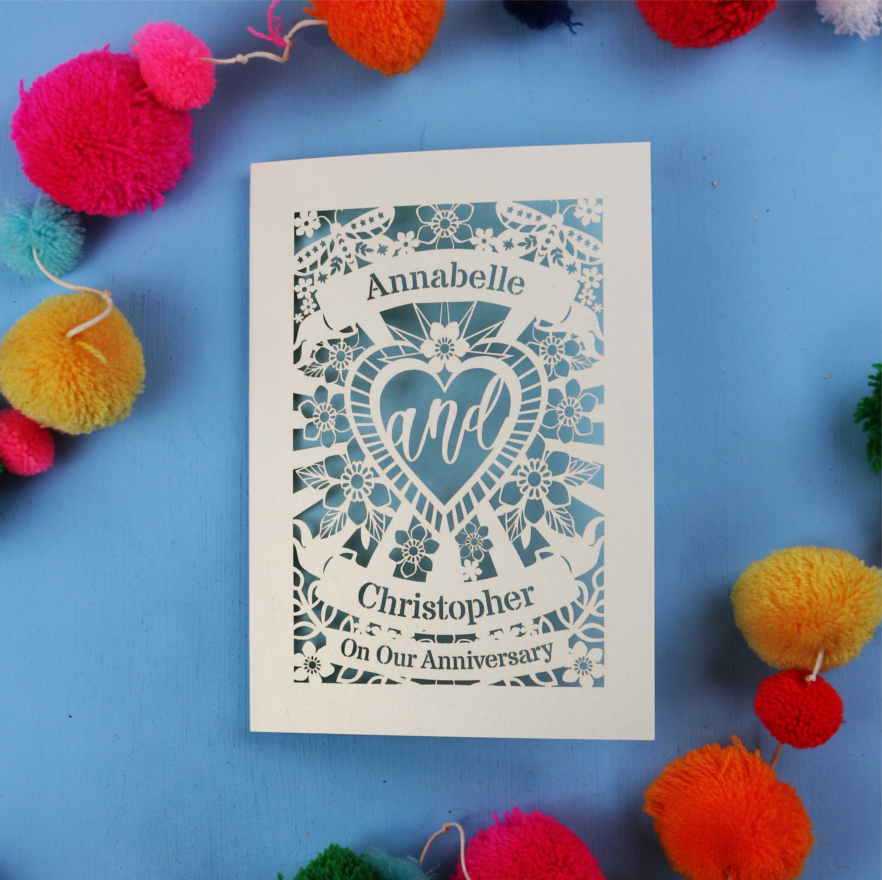 Personalised husband anniversary card with decorative heart design on a blue background with colourful pom-poms.