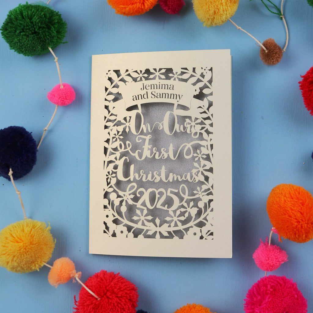 Personalized Christmas card with 'In Our First Christmas 2025' text, surrounded by colourful pom-poms on a blue background.