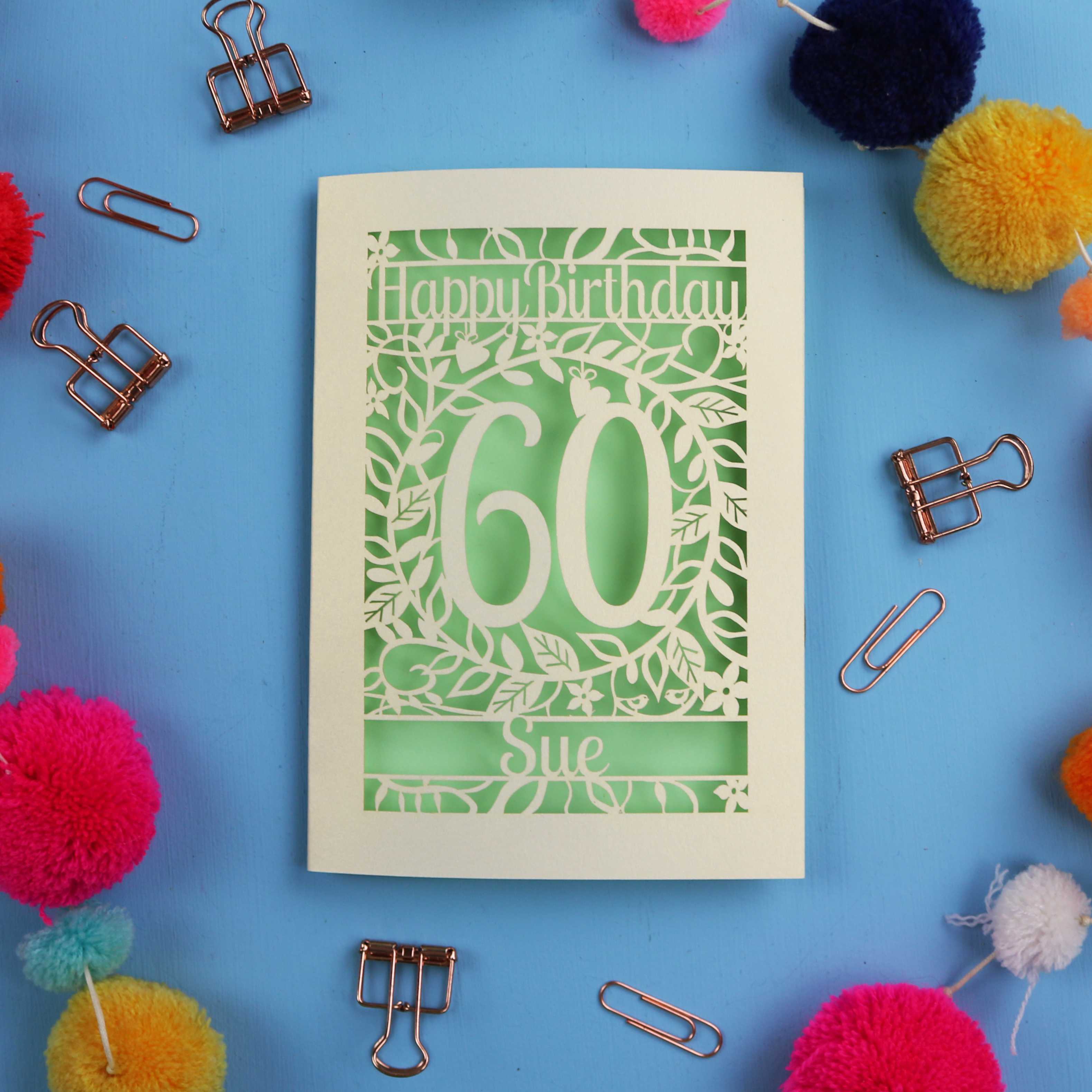 60th Birthday card with 'Happy Birthday Sue' on a blue background with colourful pom-poms and paper clips.