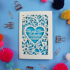 Decorative paper cut out wedding anniversary card with personalized text on a blue background with decorative items.
