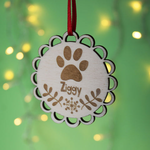 A wooden Christmas decoration engraved with a paw and a pet's name underneath.  - 