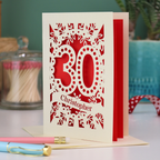 A paper cut out 30th birthday card with laser cut '30' design and personalised with the bane "Christopher" in cut out stencil writing on a banner shape.