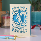 A paper cut out 30th birthday card with laser cut '30' design and personalised with the bane "Christopher" in cut out stencil writing on a banner shape.