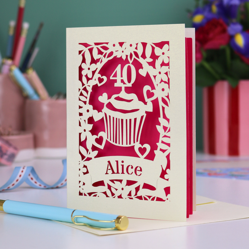 Decorative laser cut 40th birthday card with '40' and 'Alice', and a cupcake design, on a table with stationery items.