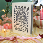A personalised laser cut 90th birthday card with a cupcake tower design and the text 'Happy Birthday Jenny', displayed on a yellow-and-white checked tablecloth with pink ribbons and lit candles in a decorated setting.