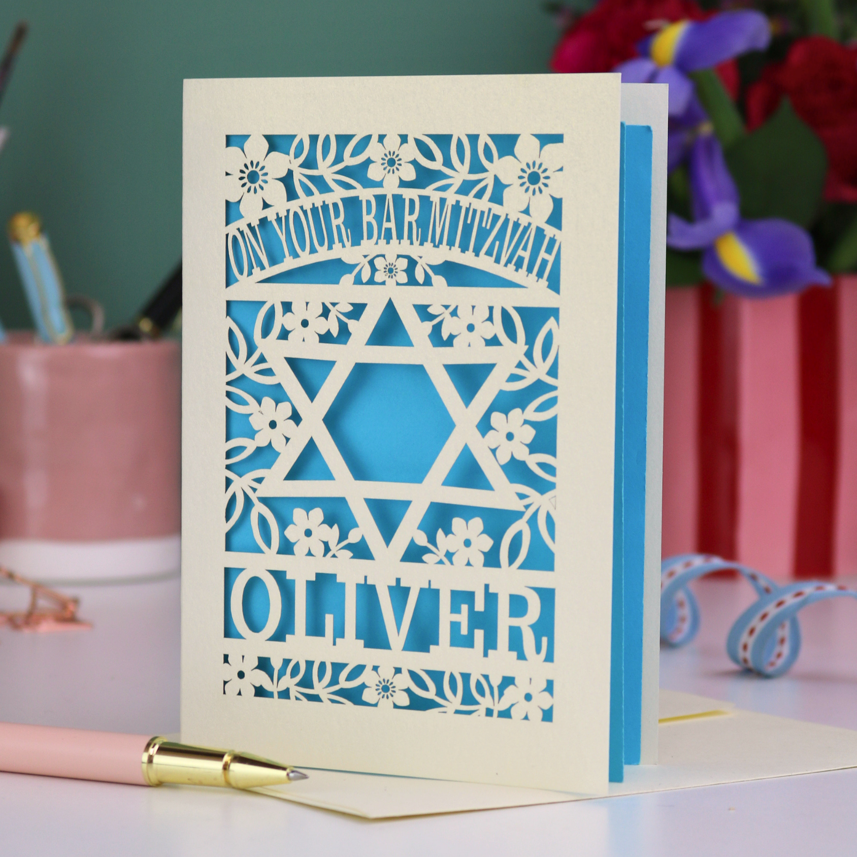 Personalized Bar Mitzvah card with laser cut star design and name 'Oliver' on a desk with stationery items.