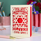Personalized Bar Mitzvah card with cut out decorative design and name 'Oliver' on a desk with stationery items.