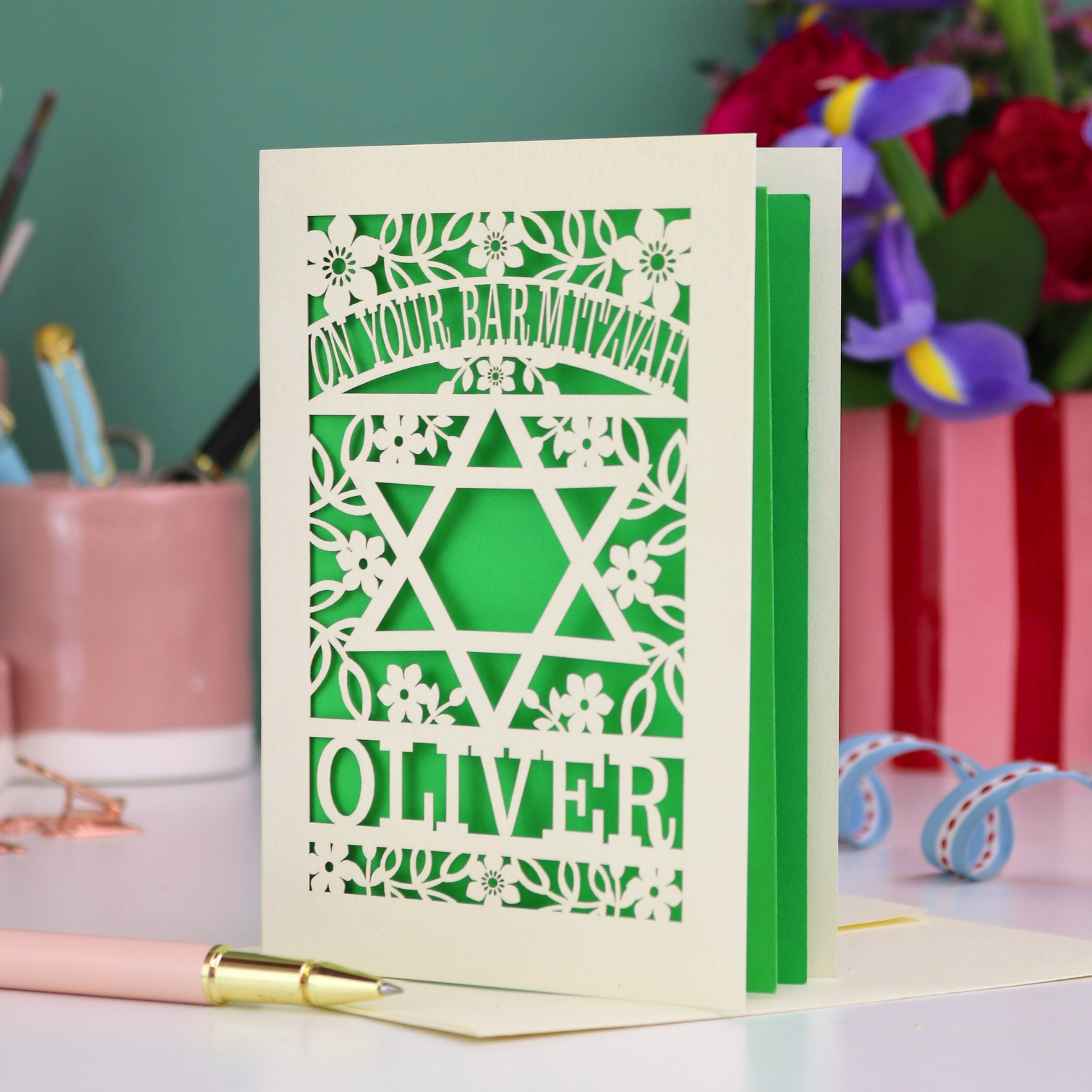 Personalized Bar Mitzvah card with Star of David design and floral patterns on a desk with stationery items.
