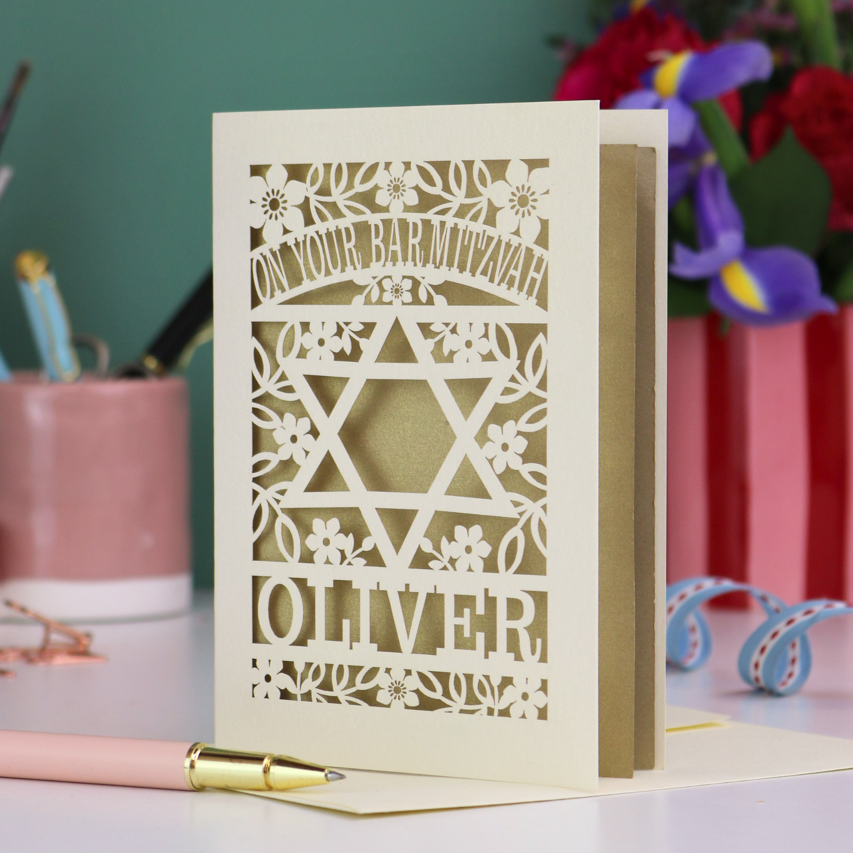 Personalized laser cut Bar Mitzvah card with floral design and text on a desk with stationery items.