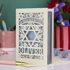 Personalized Bar Mitzvah card with star design and name 'Oliver' on a desk with stationery items.