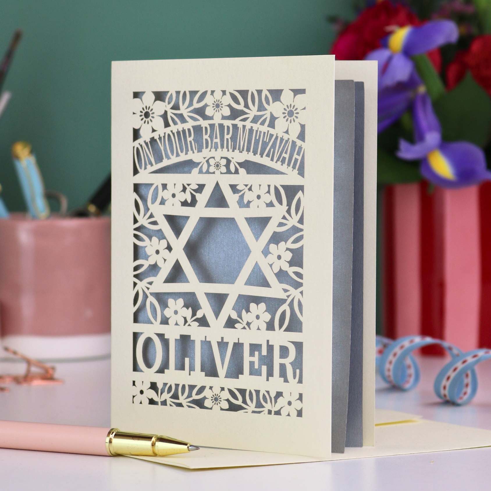 Personalized Bar Mitzvah card with star design and name 'Oliver' on a desk with stationery items.
