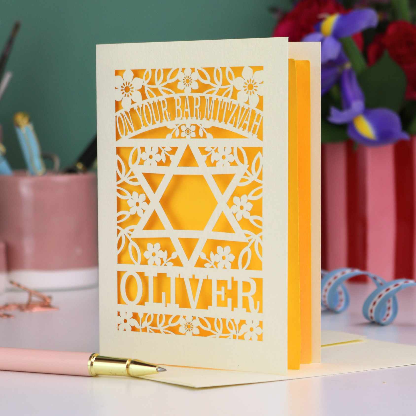 Personalised Bar Mitzvah card with paper cut star design and name 'Oliver' on a desk with stationery items.