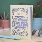 Personalised Laser cut birthday card with floral design and decorative "Happy Birthday" cut out text on a white surface with stationery items.