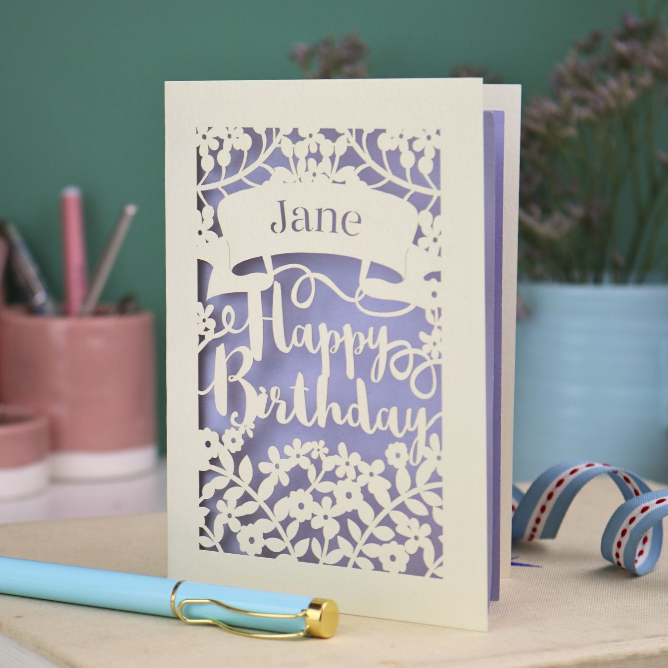 Personalised Laser cut birthday card with floral design and decorative "Happy Birthday" cut out text on a white surface with stationery items.