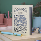 Laser cut birthday card with decorative text on a white surface with stationery items.