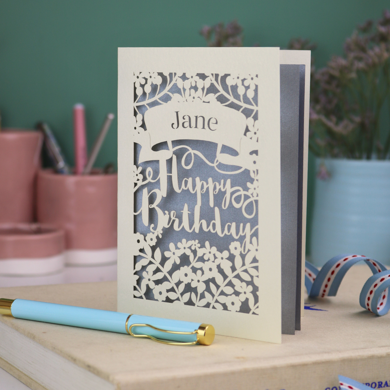 Laser cut birthday card with decorative text on a white surface with stationery items.