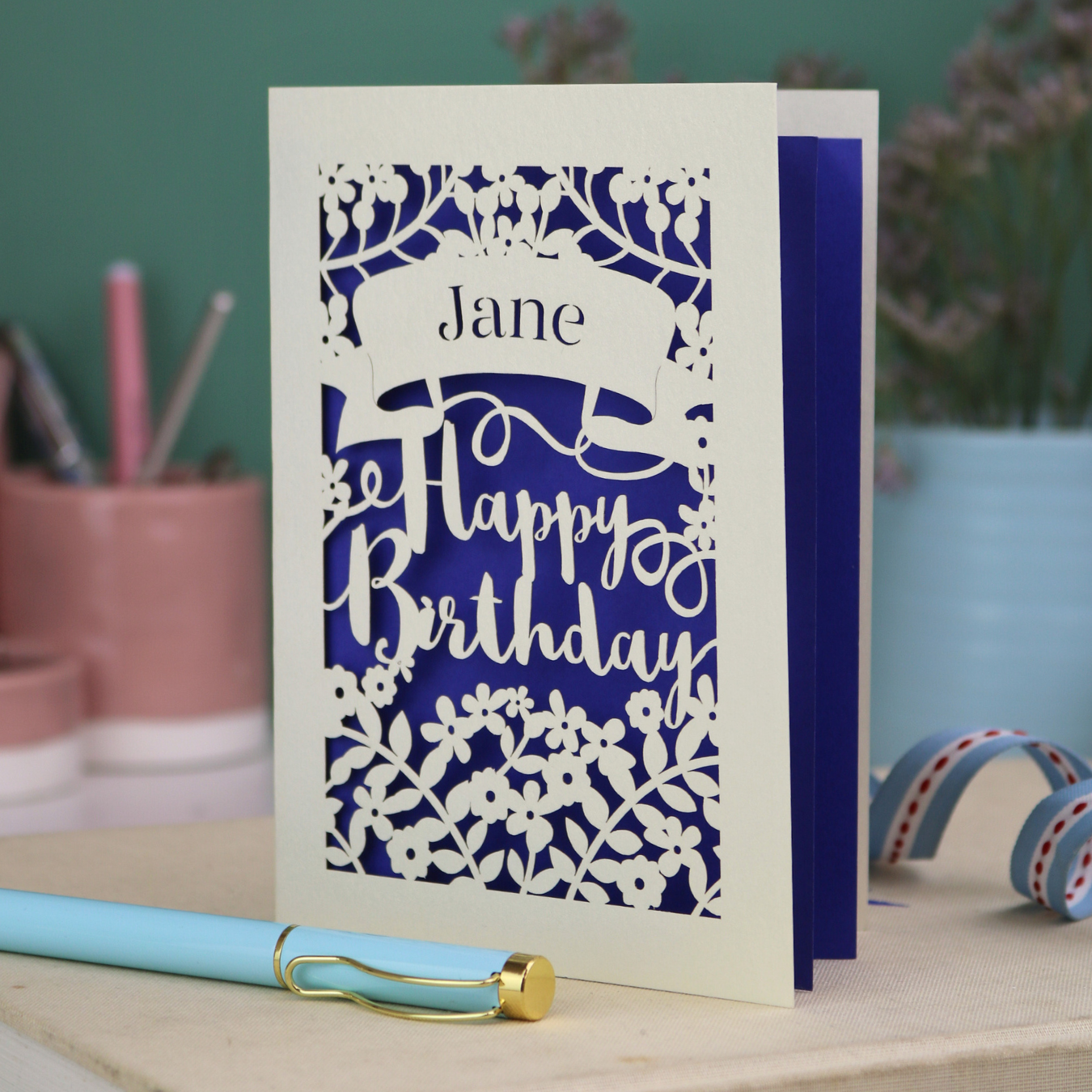 Laser cut birthday card with decorative text on a white surface with stationery items.