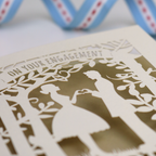 Engagement card with cut-out silhouettes of a couple and decorative elements.