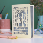 Engagement card with personalized names on a desk with stationery items.