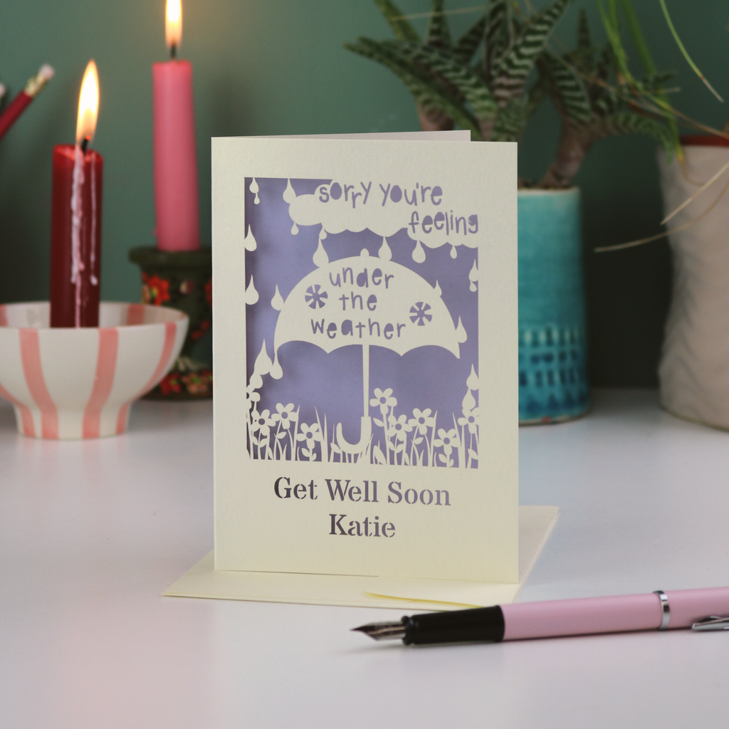 A laser cut get well soon card, with cut out umbrella design and the text 'Sorry you're feeling under the weather, get well soon' and personalised with a name.