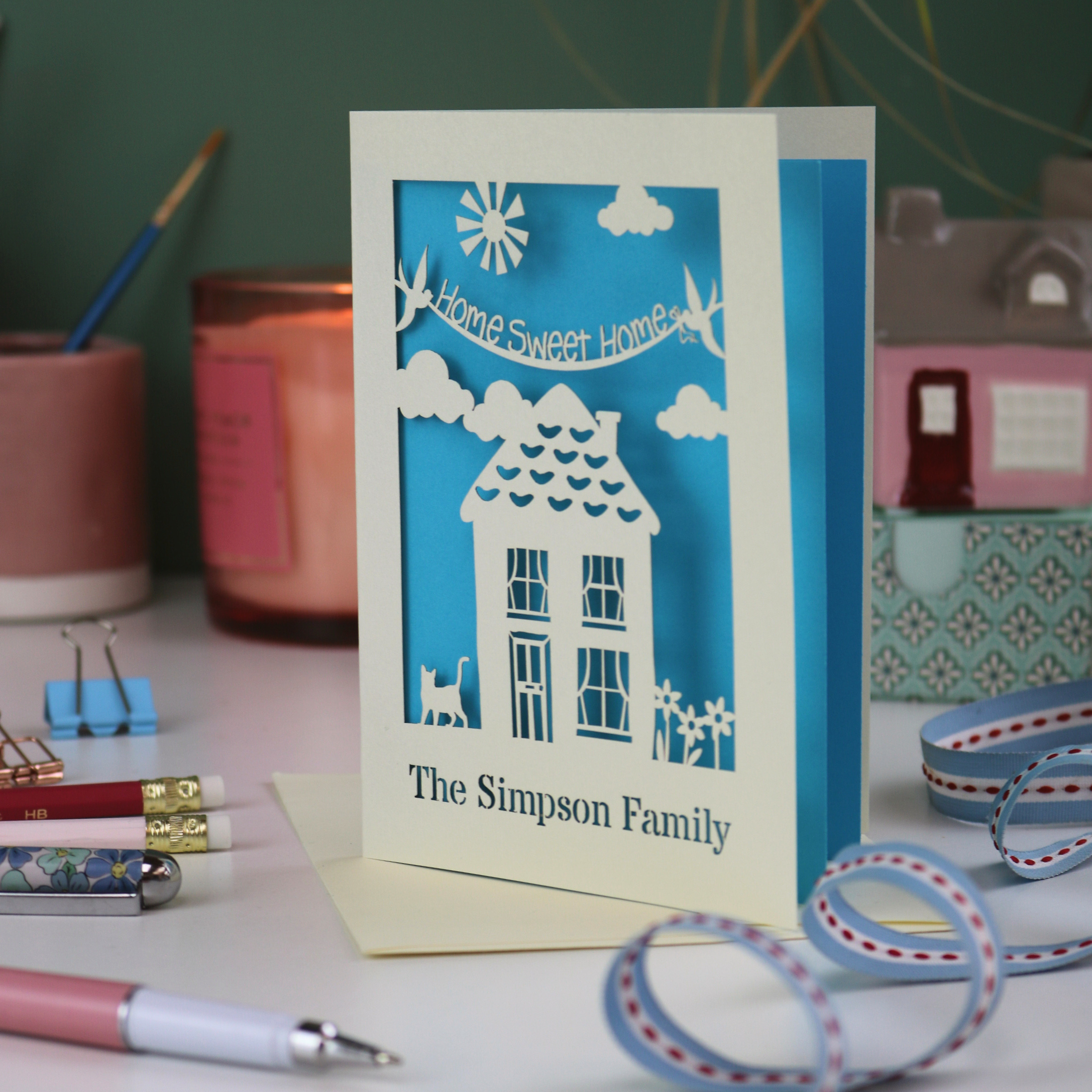 A laser cut new home card with cut out house design and the words "home sweet home" and personalised with the name of the recipients underneath