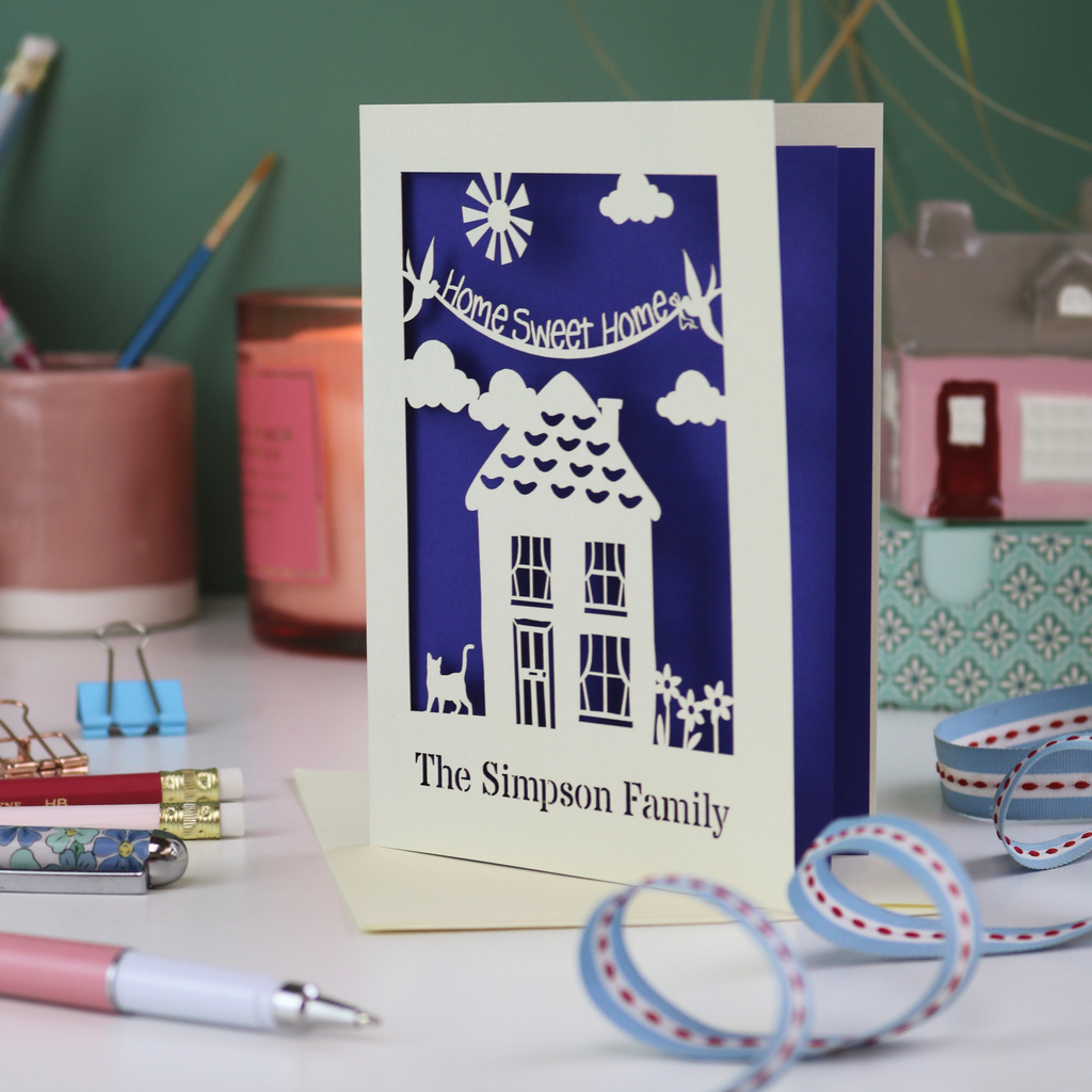 A laser cut new home card with cut out house design and the words "home sweet home" and personalised with the name of the recipients underneath
