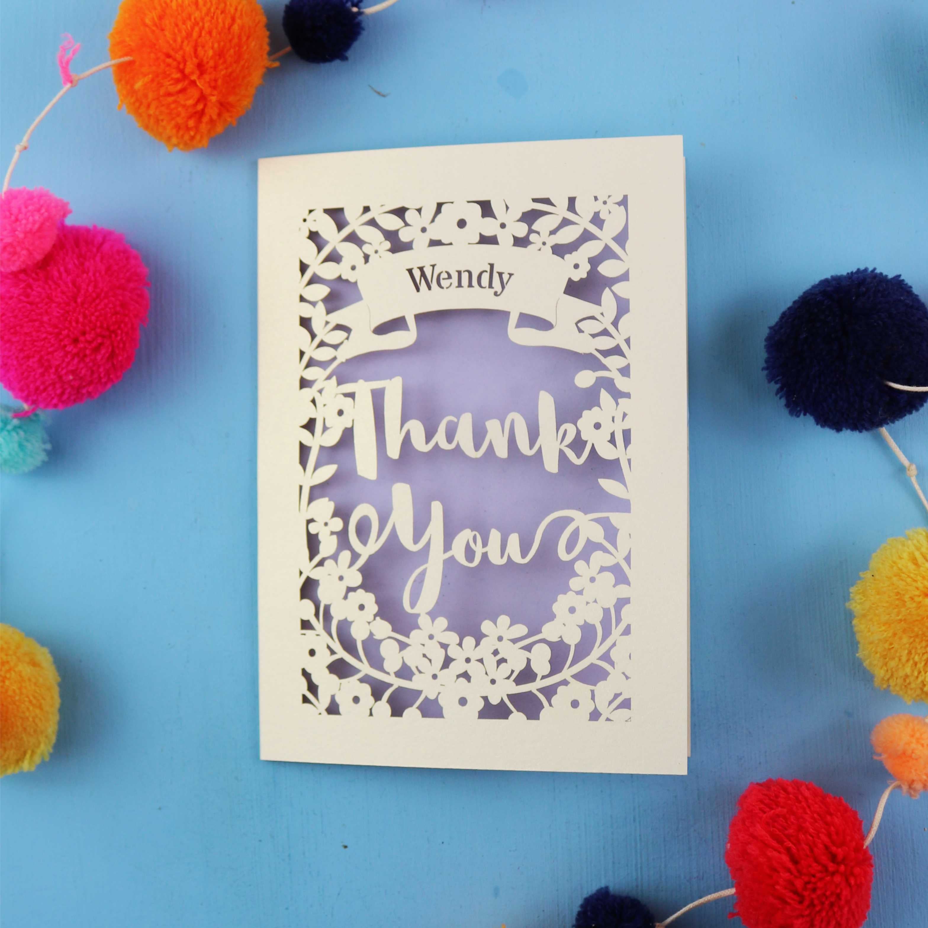 A personalised laser cut thank you card with the recipient's name in a banner and the words "Thank You" surrounded by a floral border.