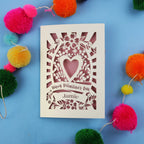 Decorative Valentine's card with floral heart design on a blue background with colourful pom-poms.