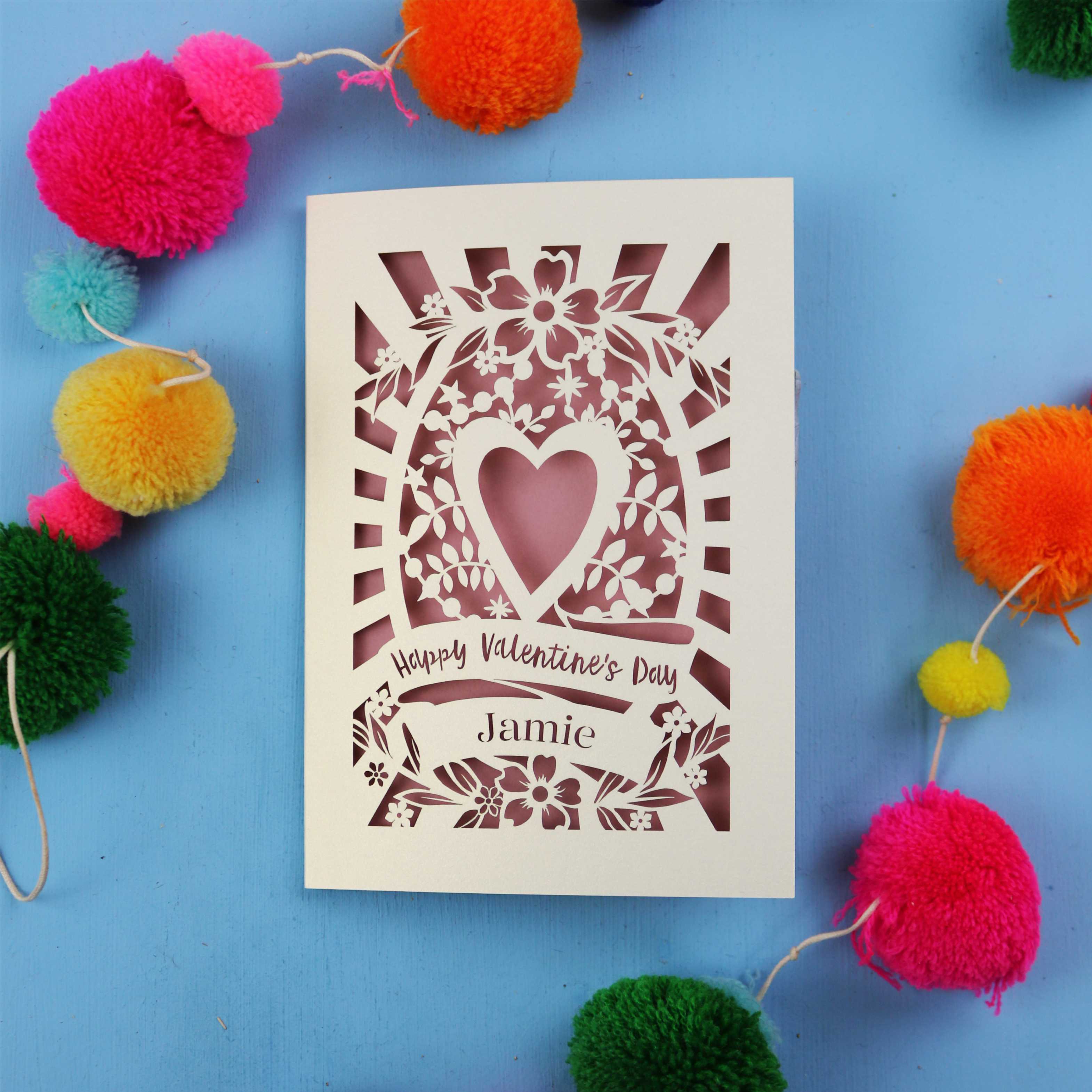 Decorative Valentine's card with floral heart design on a blue background with colourful pom-poms.