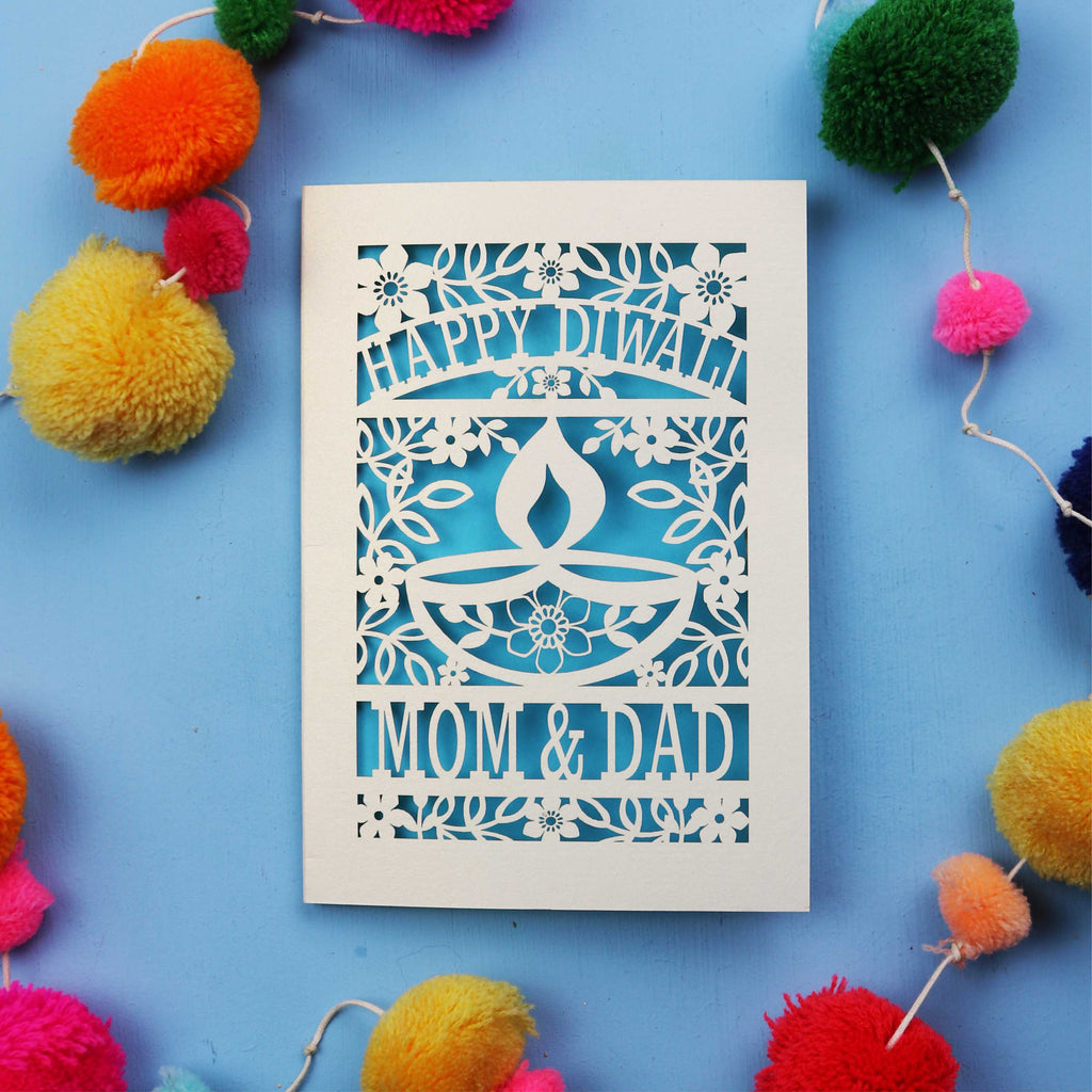 Decorative Diwali card with 'Happy Diwali' and 'Mom & Dad' text on a blue background with colourful pom-poms.