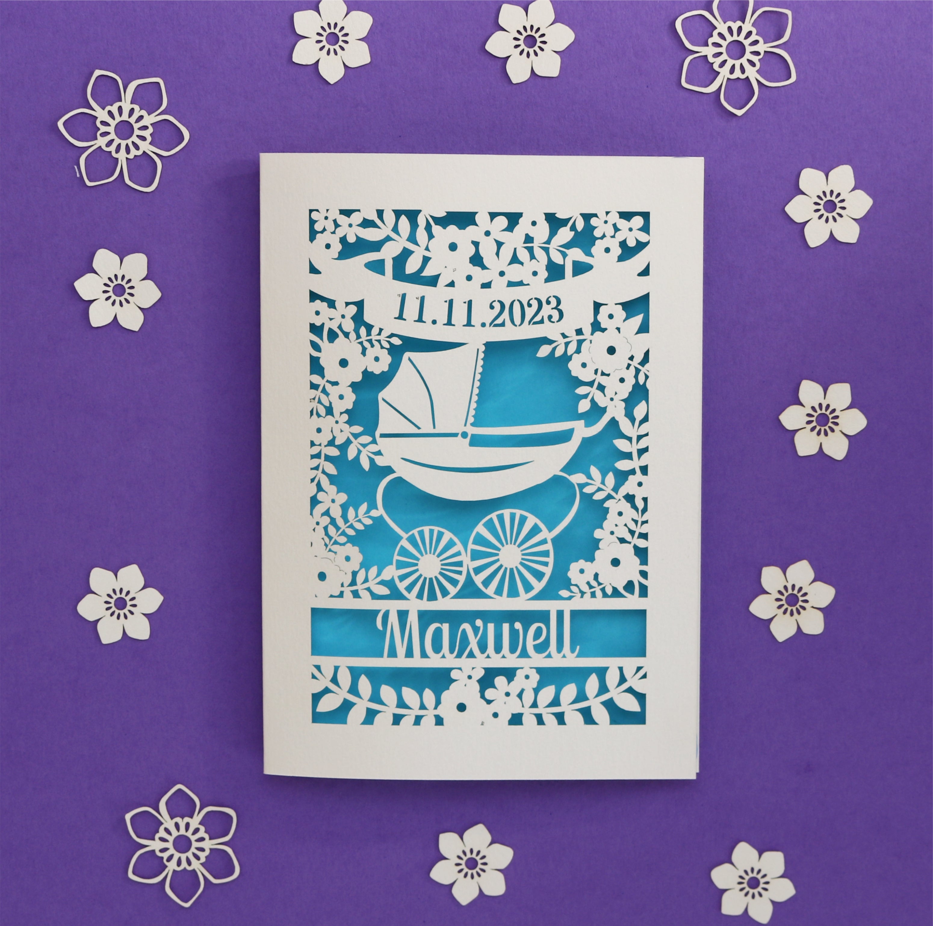 A personalised card for a new baby, laser cut and featuring a vintage pram surrounded by flowers. Card is personalised with date of birth and baby's name.