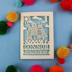 Laser Cut 1st Birthday card with ship design and 'CONNOR' text on a blue background with colourful pom-poms.