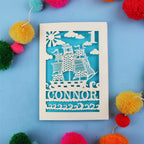 Decorative 1st Birthday card with ship design and 'CONNOR' text on a blue background with colourful pom-poms.