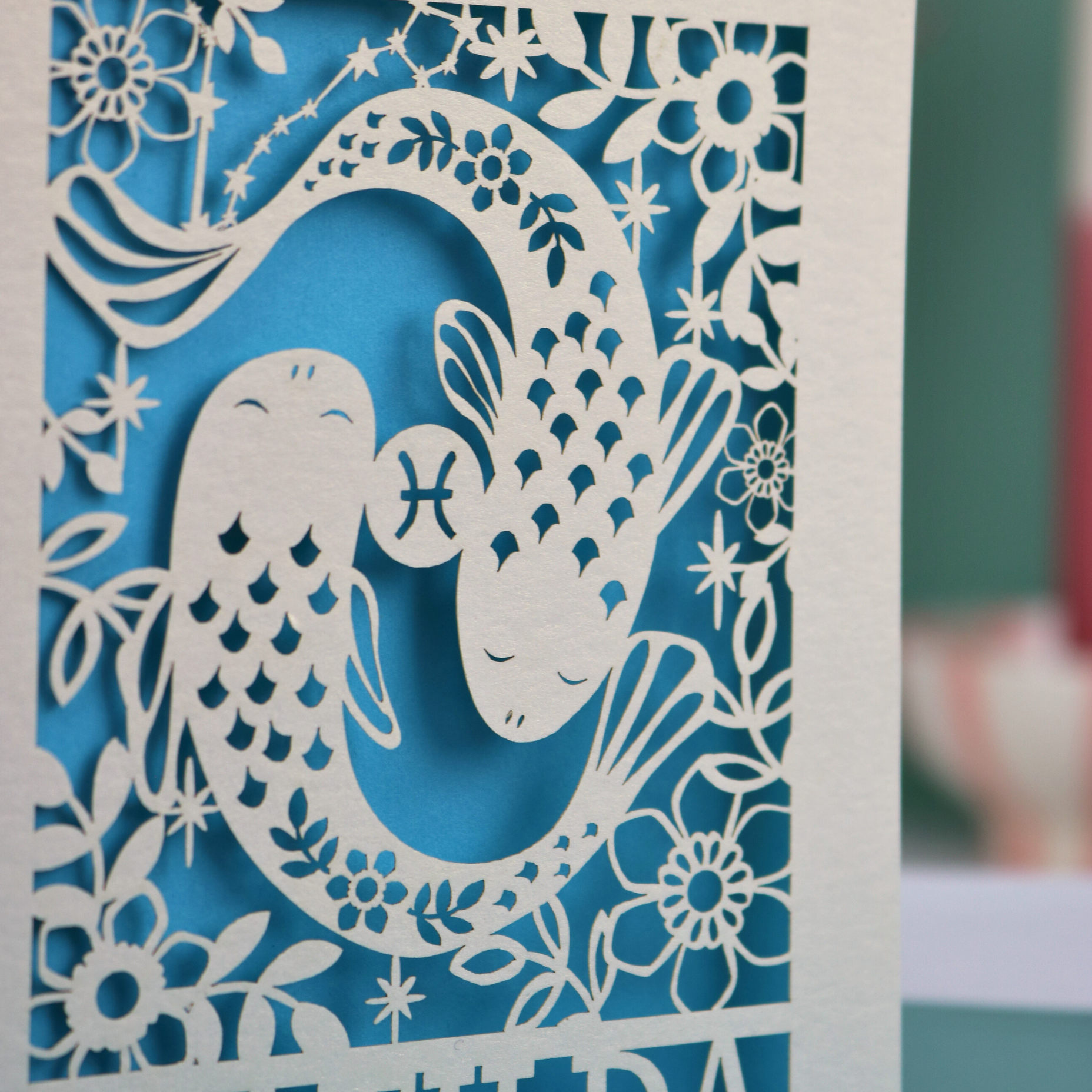 Decorative paper cut out of a Pisces fish design with floral elements on a blue background