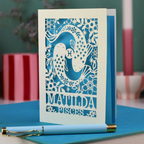 Decorative Pisces birthday card with 'Matilda' and a laser cut Pisces design on a blue surface with a pen.
