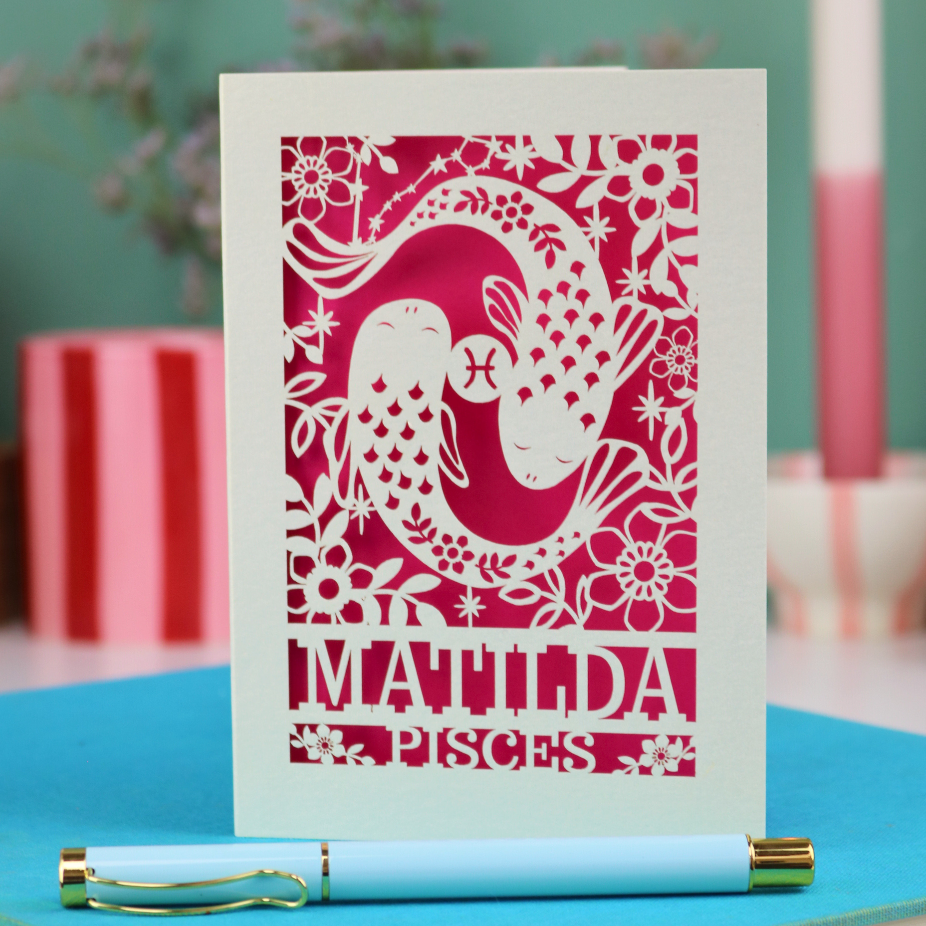 Decorative Pisces birthday card with 'Matilda' and a laser cut Pisces design on a blue surface with a pen.