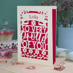 A personalised congratulations on your success card with 'Lola, so very proud of you' text on a decorative surface with flowers and stationery items.