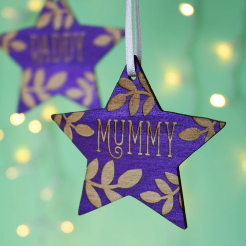 Purple star personalised Christmas decorations hanging in front of a green background with fairy lights - 