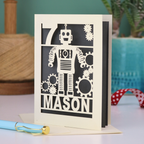 A cream and grey laser cut birthday card with robot design and personalised with the age and name of the recipient