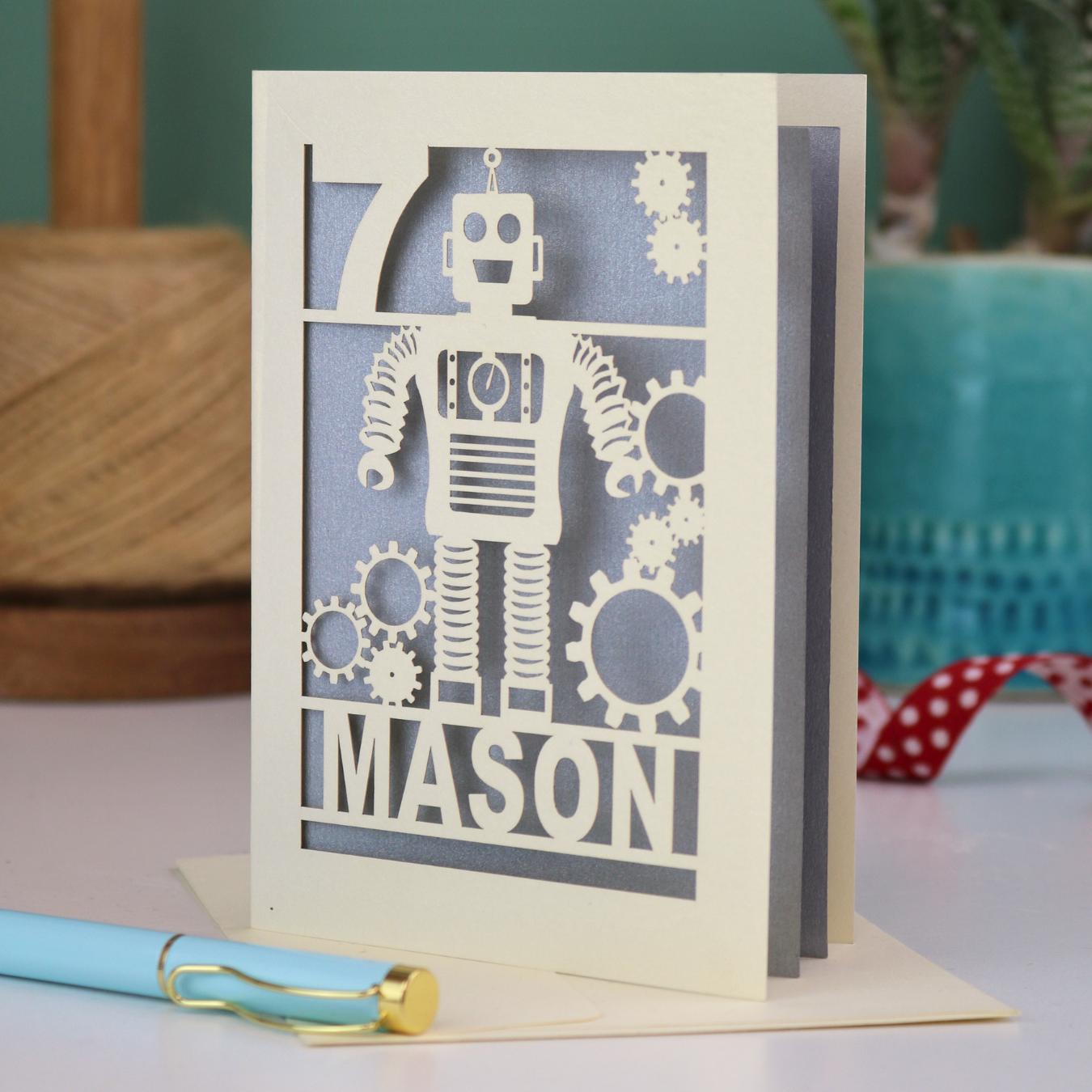 A cream and silver laser cut birthday card with robot design and personalised with the age and name of the recipient