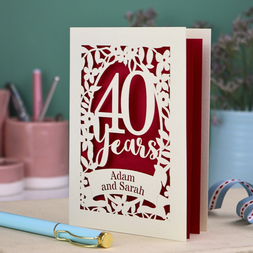 Ruby anniversary Card with '40 Years' and 'Adam and Sarah' text on a desk with stationery items.