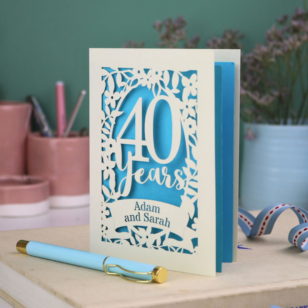 Wedding anniversary card with '40 Years' design on a wooden surface with stationery items.