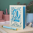 Wedding anniversary card with '40 Years' design on a wooden surface with stationery items.