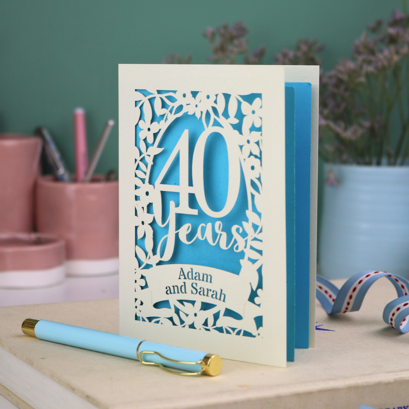 Wedding anniversary card with '40 Years' design on a wooden surface with stationery items.